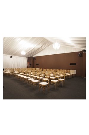 a large white tent with rows of tiffany chairs gold
